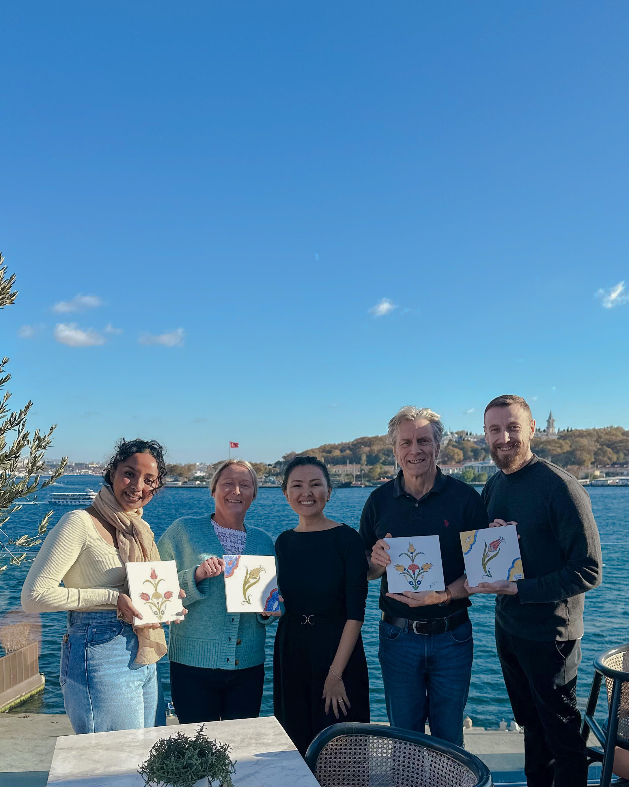 Art collaborations with hotels and stays Group of people holding painted ceramic tiles, on the terrace of the hotel